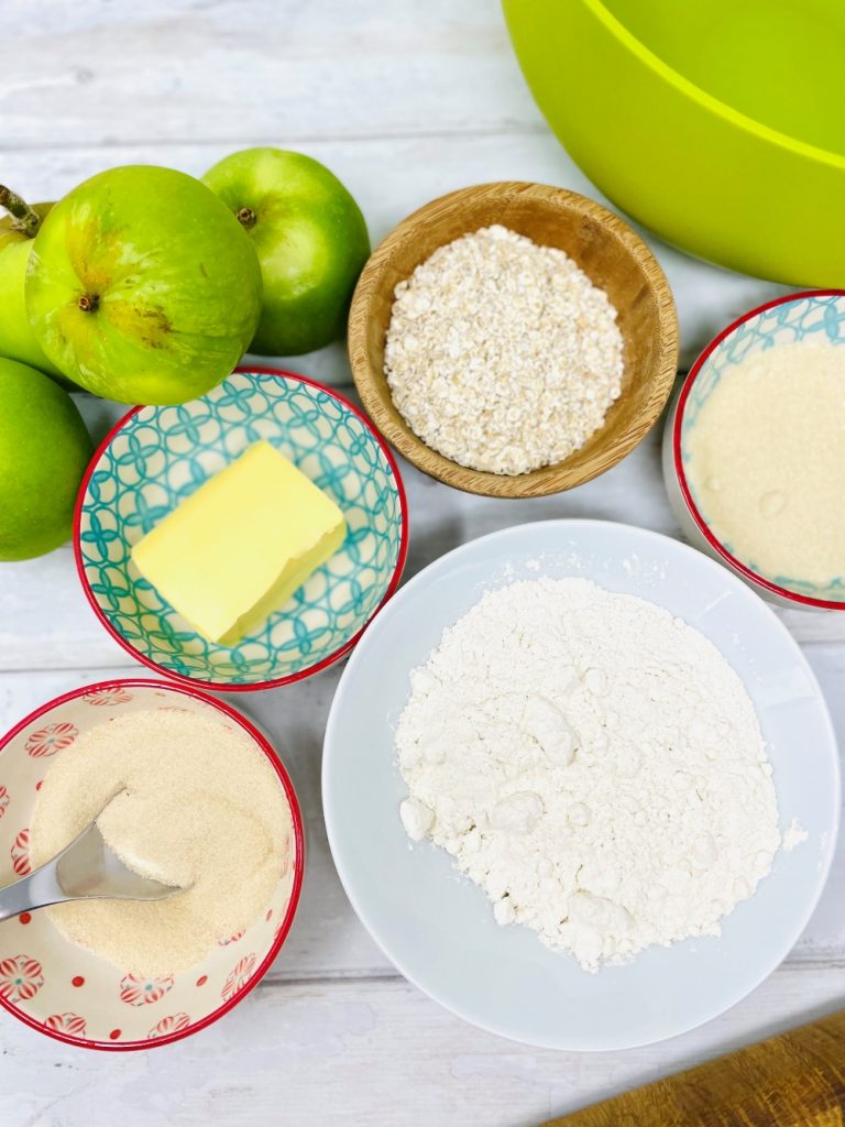 apple crumble ingredients on a table - bramley apples, butter, sugar, cinnamon, oats, plain flour