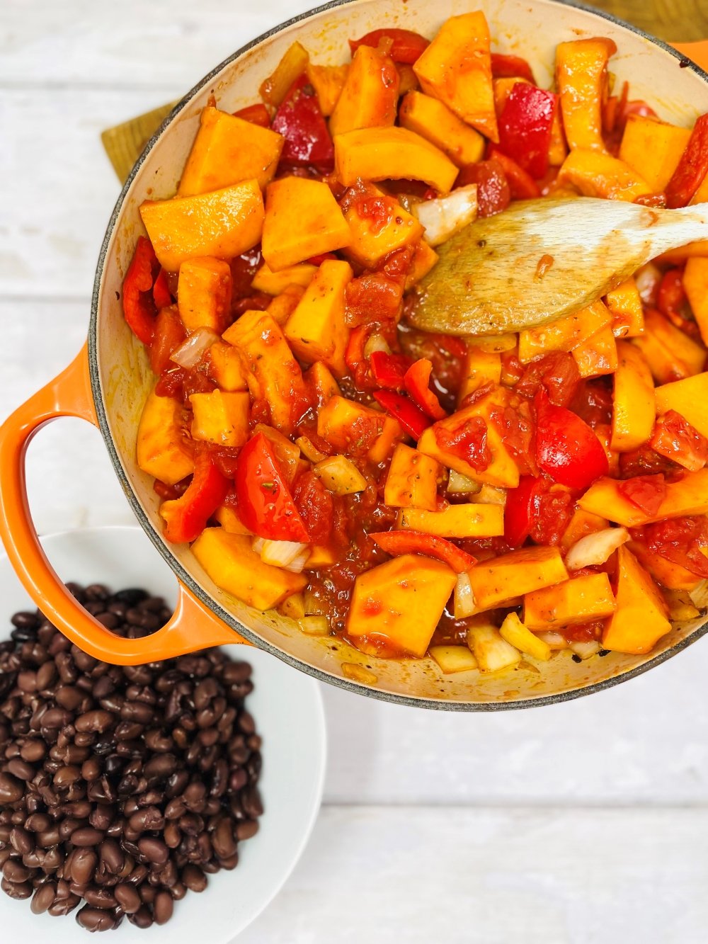 making butternut squash chilli in a skillet pan being stirred with a wooden spoon