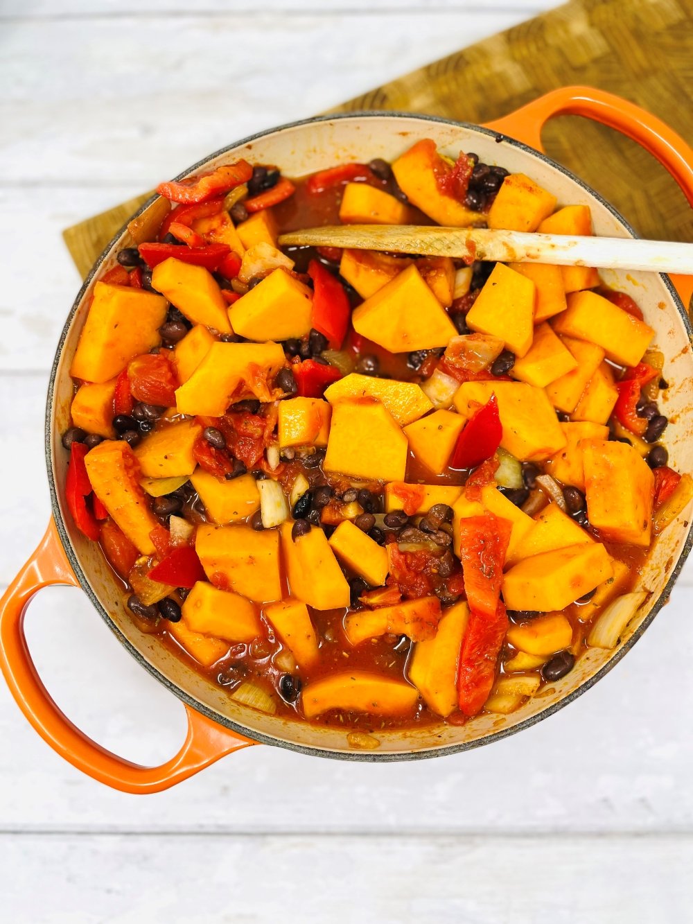 stirring a squash an black bean chilli in a skillet pan