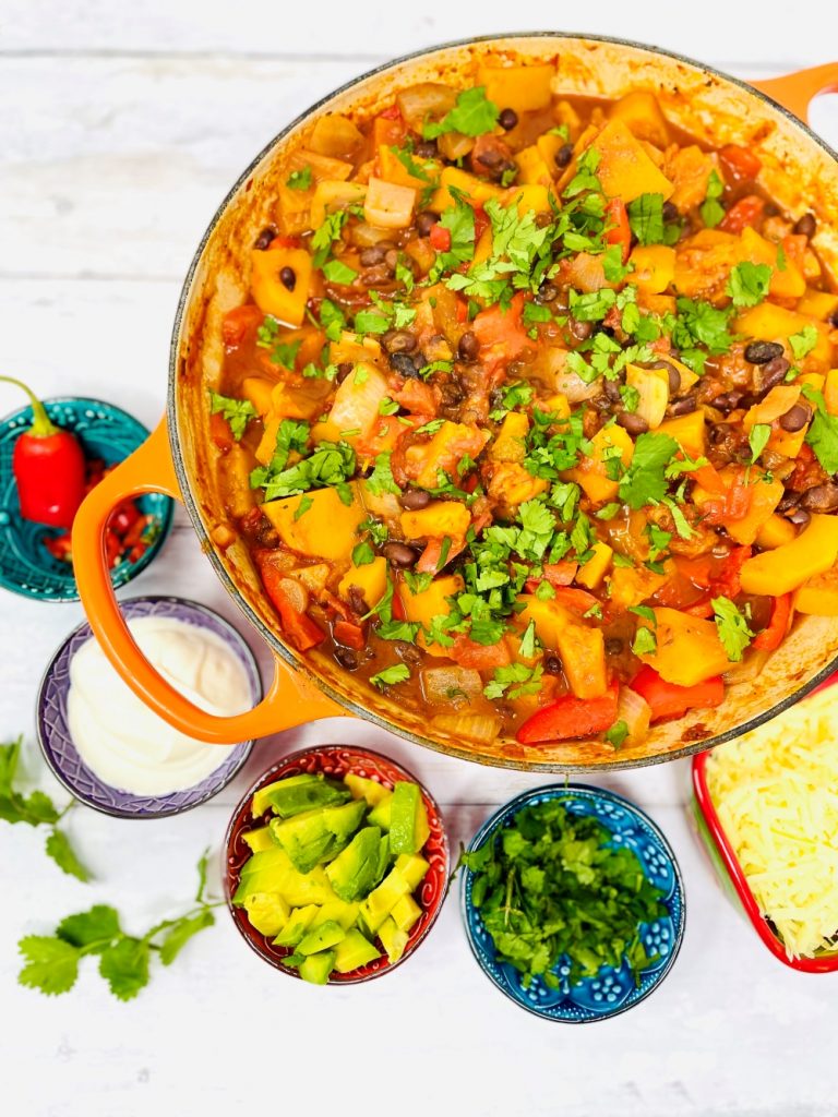 butternut squash chilli veggie chilli recipe served with side dishes of coriander, avocado chunks, yogurt, sliced chillies, blue corn tortillas and grated cheese