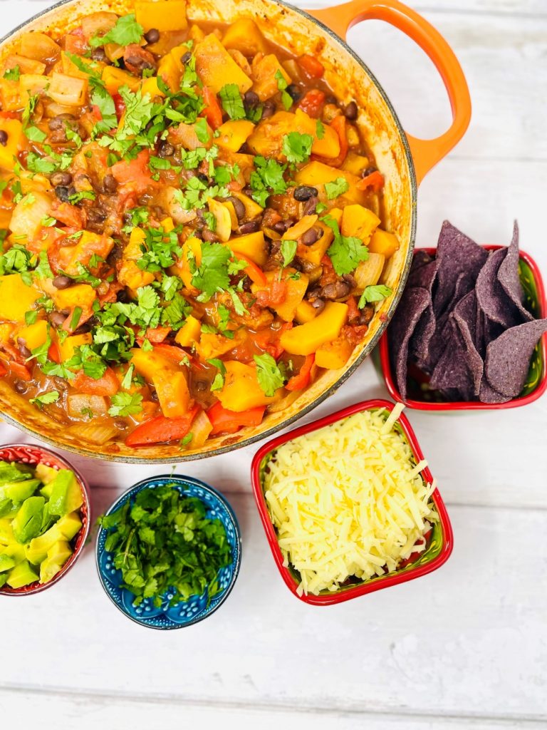butternut squash chilli veggie chilli recipe served with side dishes of coriander, avocado chunks, yogurt, sliced chillies, blue corn tortillas and grated cheese