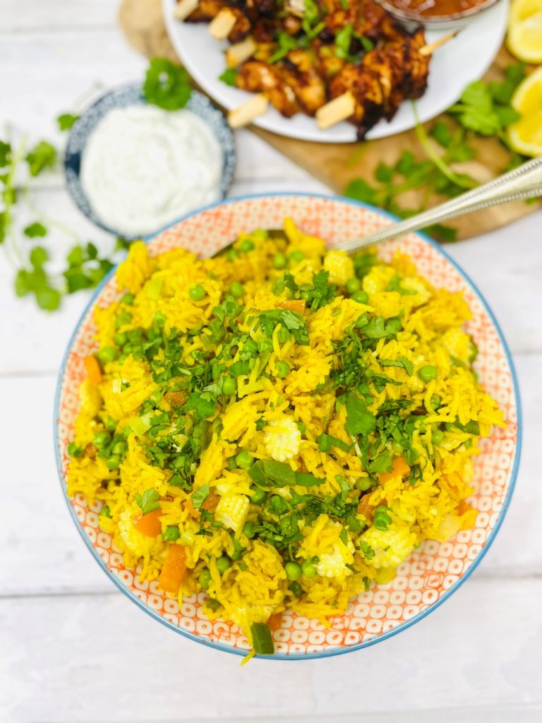 savoury rice golden vegetable rice in a serving bowl scattered with chopped coriander