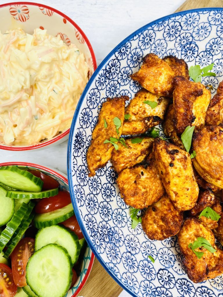 serving bowl with paprika chicken in it. Next to a bowl of coleslaw, tomato and cucumber salad