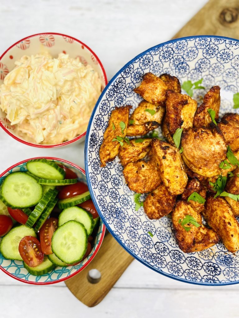 serving bowl with paprika chicken in it. Next to a bowl of coleslaw, tomato and cucumber salad