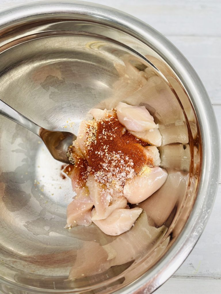 paprika, garlic and onion granules tipped onto raw chicken breast in a mixing bowl