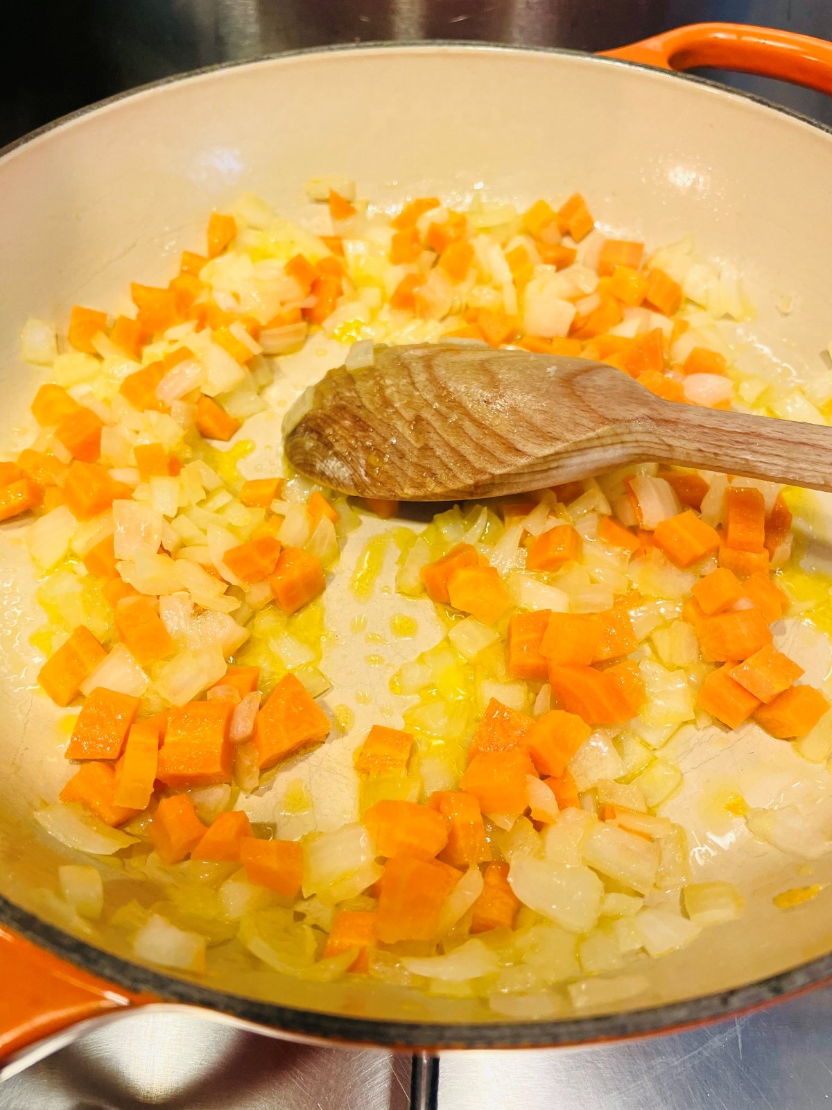 diced carrots and onions being fried in a skillet pan stirred with a wooden spoon