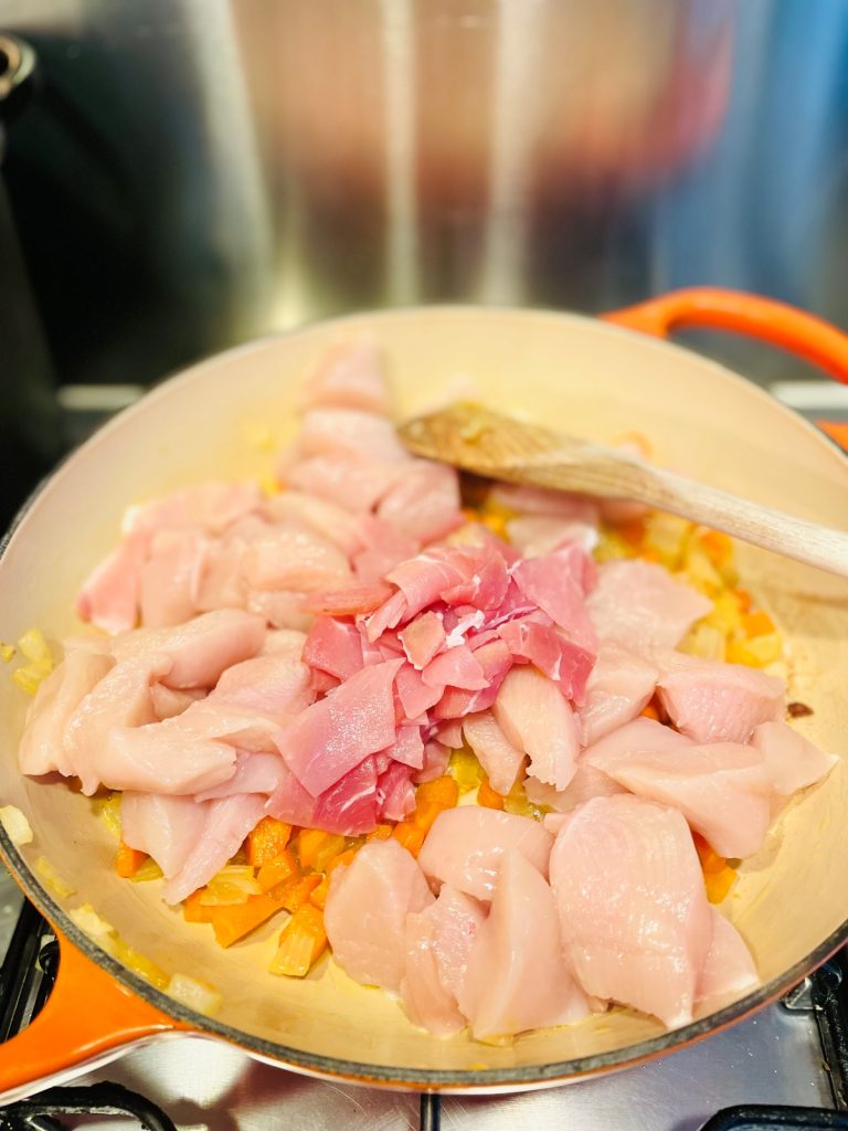 diced chicken and bacon added to a pan with carrots and onions