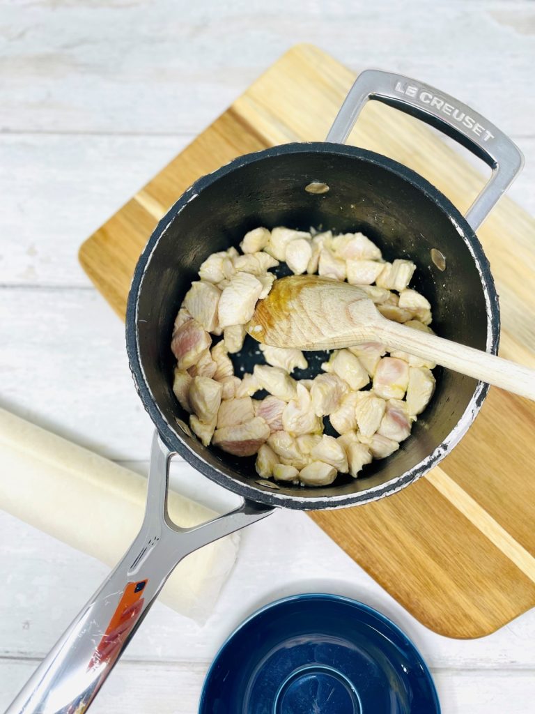 chicken breast pieces in a saucepan being stirred with a wooden spoon