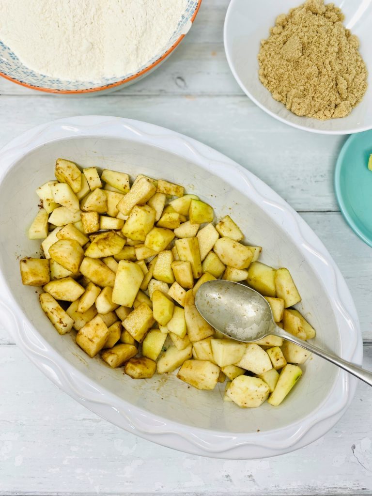 peeled and diced pear tossed with brown sugar in an ovenproof dish - bowl of flour, brown sugar in the background.